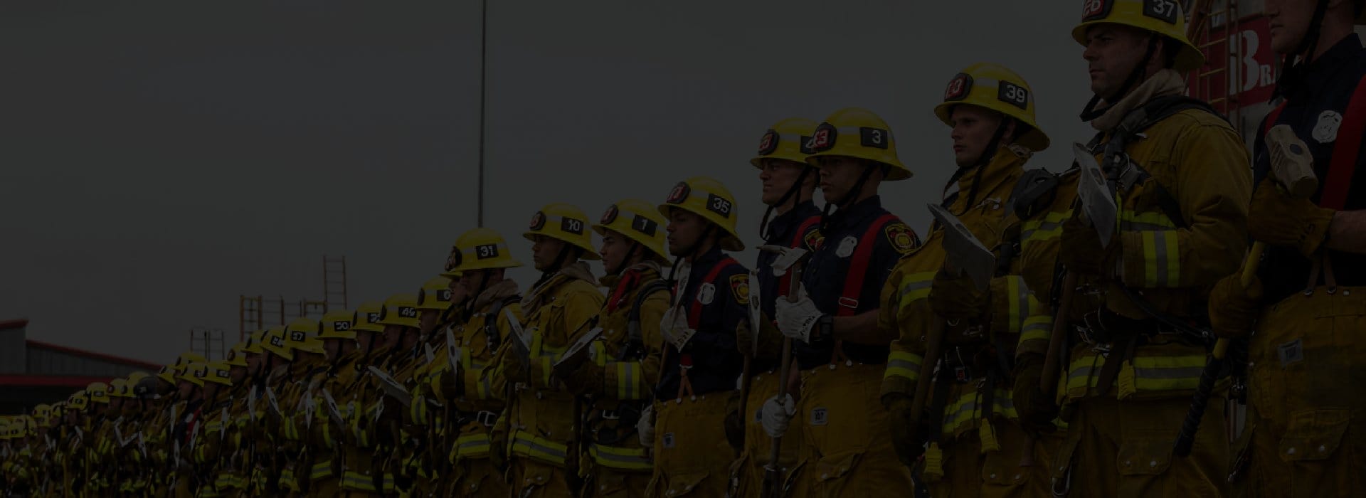 A line of firemen standing at attention, holding axes