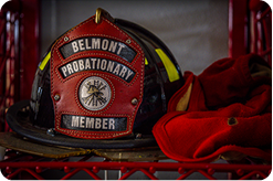 A Belmont Probationary Member fire helmet on a red wire shelf, with a red cloth next to it