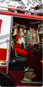 Fire engine viewed from the side, with the door open, and a firefighters helmet and gear visible inside.
