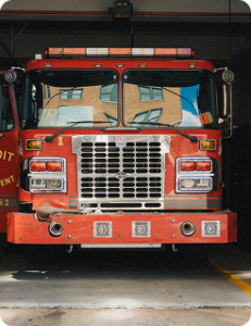 A red firetruck parked inside the garage at a station. A building is reflected in the windshield, and the passenger door is open