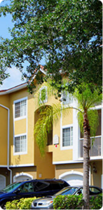 a phot oof a yellow apartment building, with cars parked and trees covering part of the view