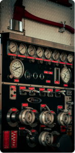 A photo of hose connections and pressure gages, with a fire axe hanging above them