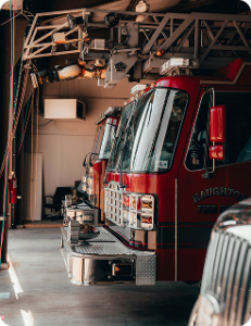 An interior photo of three fire engines in their bays, with the doors open. The engine closest to the viewer has only it's grille visible.