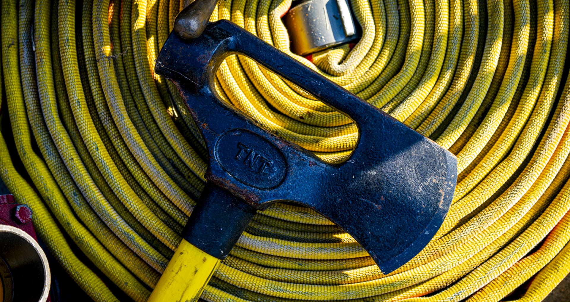 a firemans axe laid on top of a yellow coiled firehose