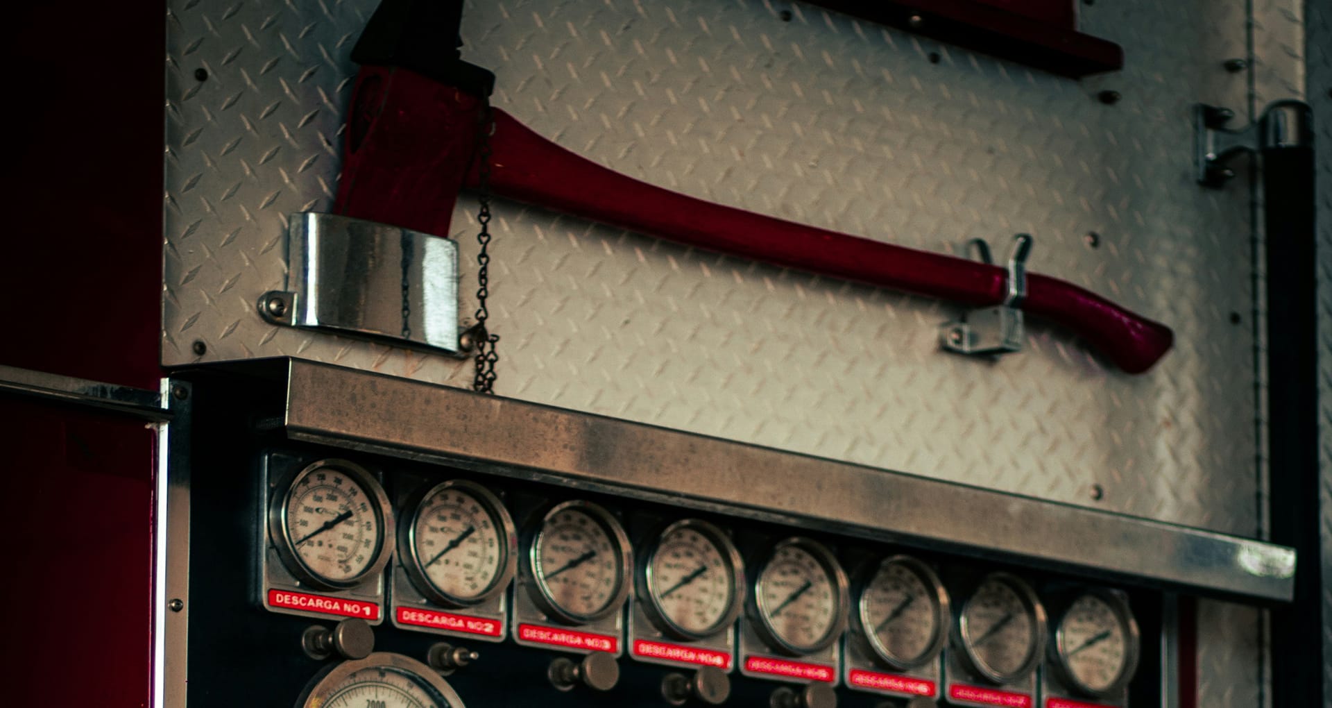 A fire axe stored safely in it's compartment on a fire engine, with pressure gages visible at the bottom of the image