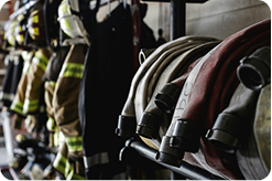 A view of a kit room, with helmets, jackets, pants and boots visible, and fire hoses in the foreground closest to the camera