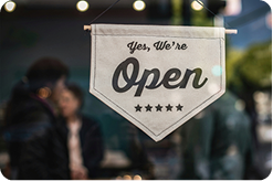 a sign hanging in a window that says "Yes, We're Open", two people in the background are visible, but out of focus.