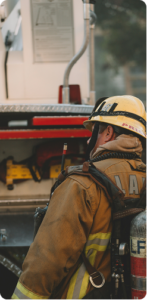 a cropped photo of a LAFD fireman in full gear, outside, with a large vehicle in front of him.