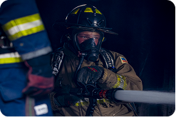 Firefighter in full gear manning a fire hose, spraying something out of view