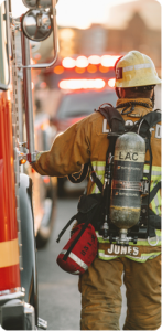 Firefighter in full gear facing away from the view, with part of a dire engine visible next to him