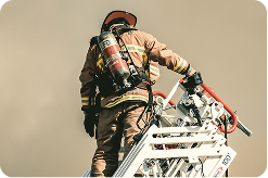 A firefighter on the aerial ladder, looking down. Heavy smoke obscures the background