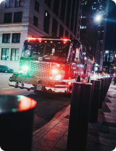Fire engine with lights on in a city street at night, with tall buildings visible behind it