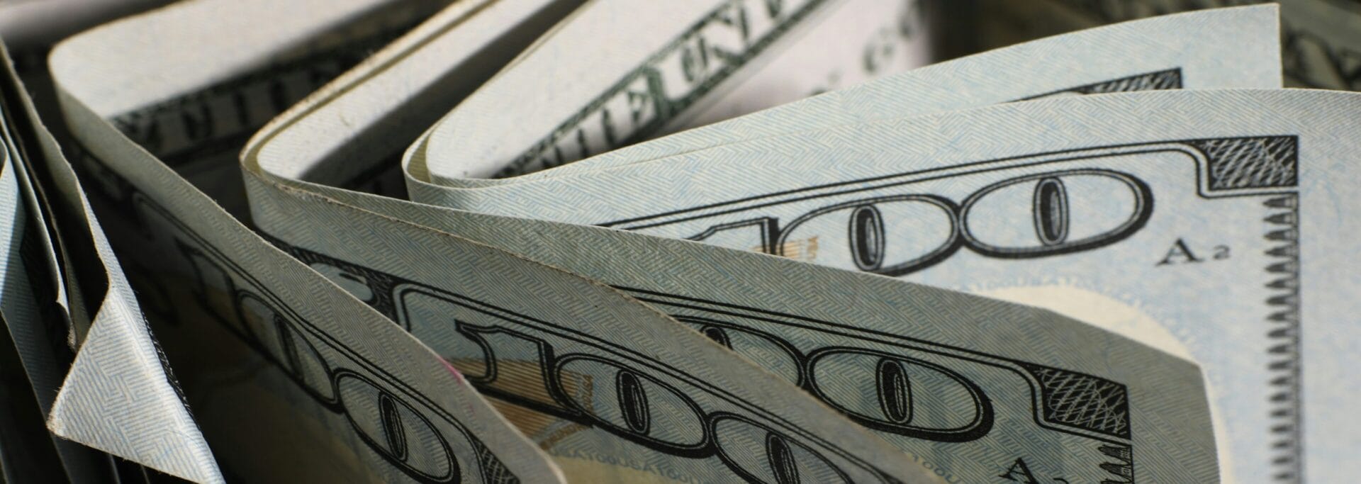 Close-up of fanned US hundred dollar bills against a dark background