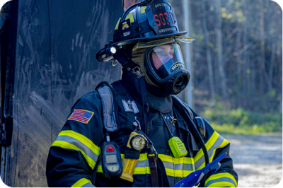 Firefighter in full protective gear including SCBA mask and helmet with South Greenville insignia at an outdoor incident scene