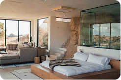 Modern bedroom with a low platform bed, glass wall, and stone accent, overlooking a scenic outdoor landscape.