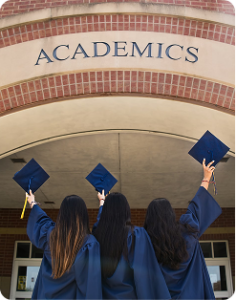 Three graduates in caps and gowns raise diplomas beneath an arched entrance labeled “ACADEMICS.”
