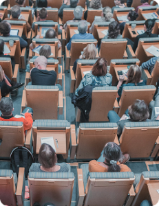 Lecture hall filled with people seated in rows of desks, facing the front of the room.