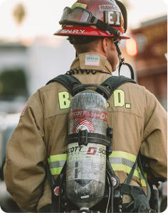 Firefighter seen from behind wearing a helmet and air tank, with reflective “BFD” lettering on the jacket.
