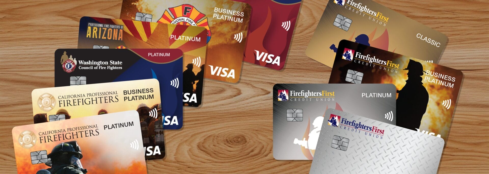 Collection of Firefighters First Credit Union Visa credit cards spread on a wood surface including Platinum, Classic, Business Platinum, and union-branded designs