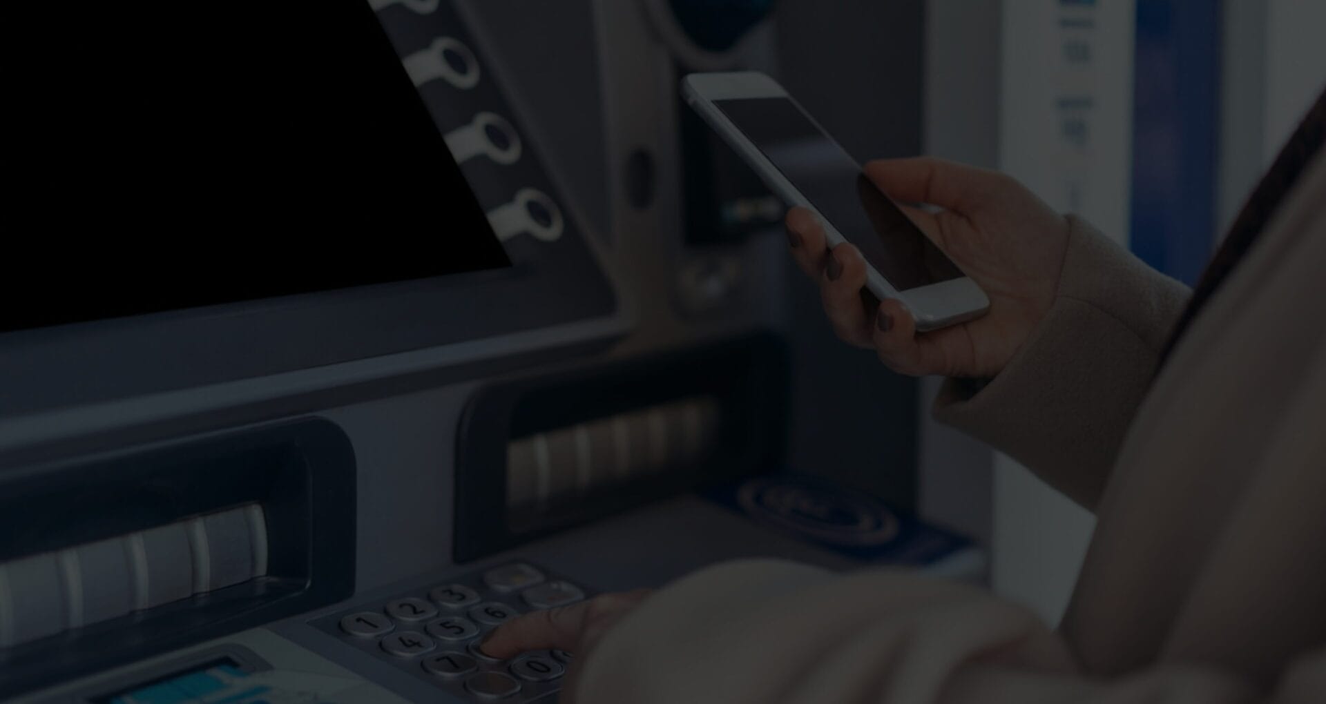 Person using a smartphone while entering a PIN at an ATM