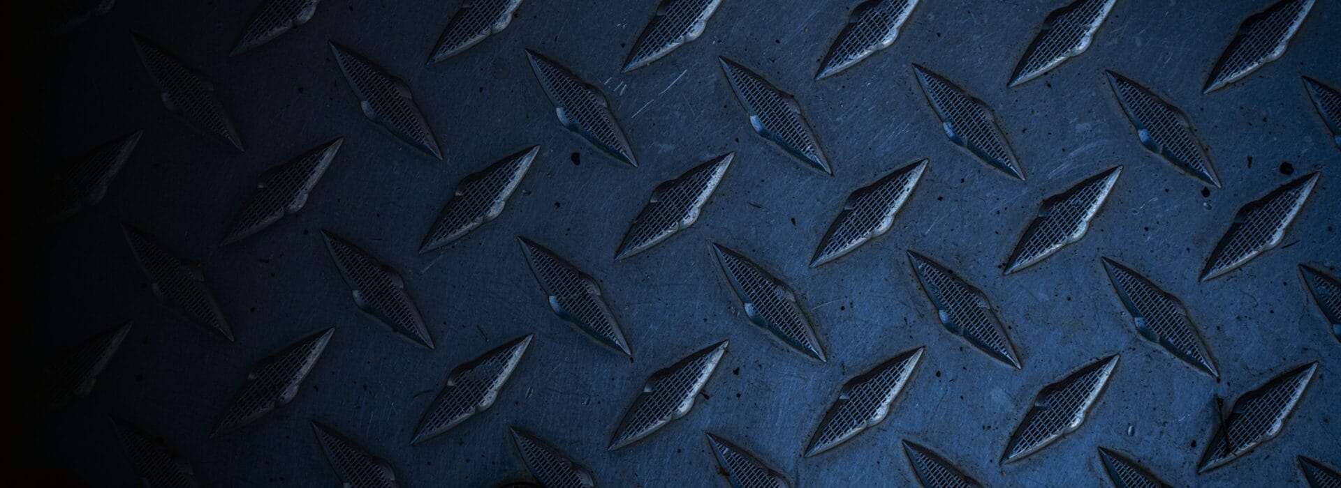 Close-up of dark blue metal diamond plate with raised, textured diamond patterns, commonly used for industrial flooring or surfaces to provide extra grip and prevent slipping