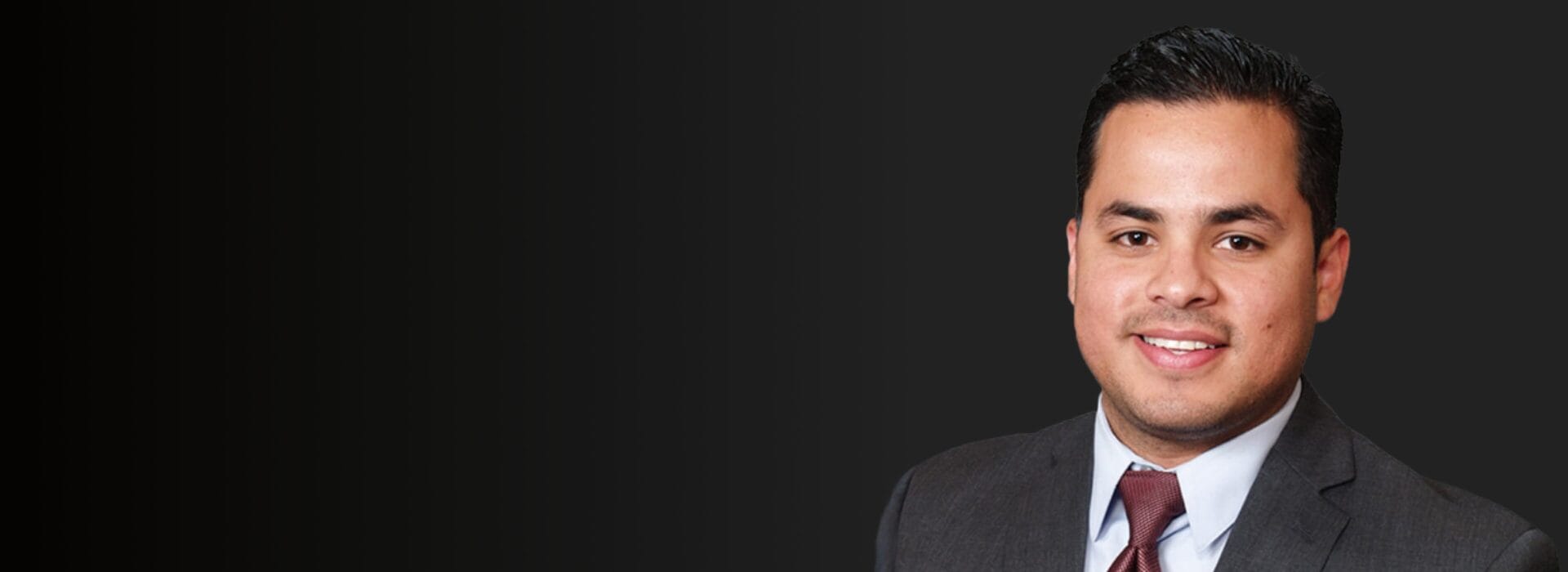 Professional headshot of Pedro Cisneros in a dark suit and burgundy tie smiling against a dark background