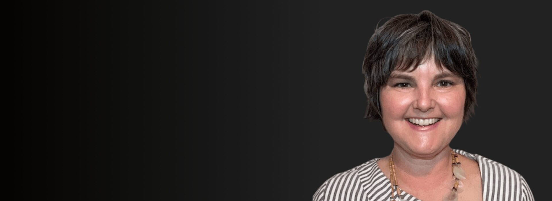 Professional headshot of Kim Stirling in a striped top and beaded necklace smiling against a dark background