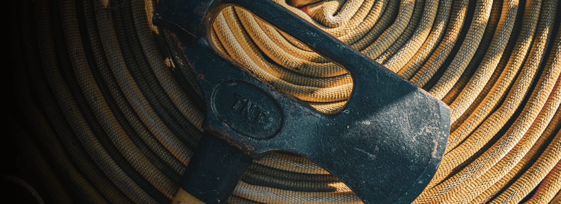 A well-worn firefighter's axe resting on a coiled fire hose