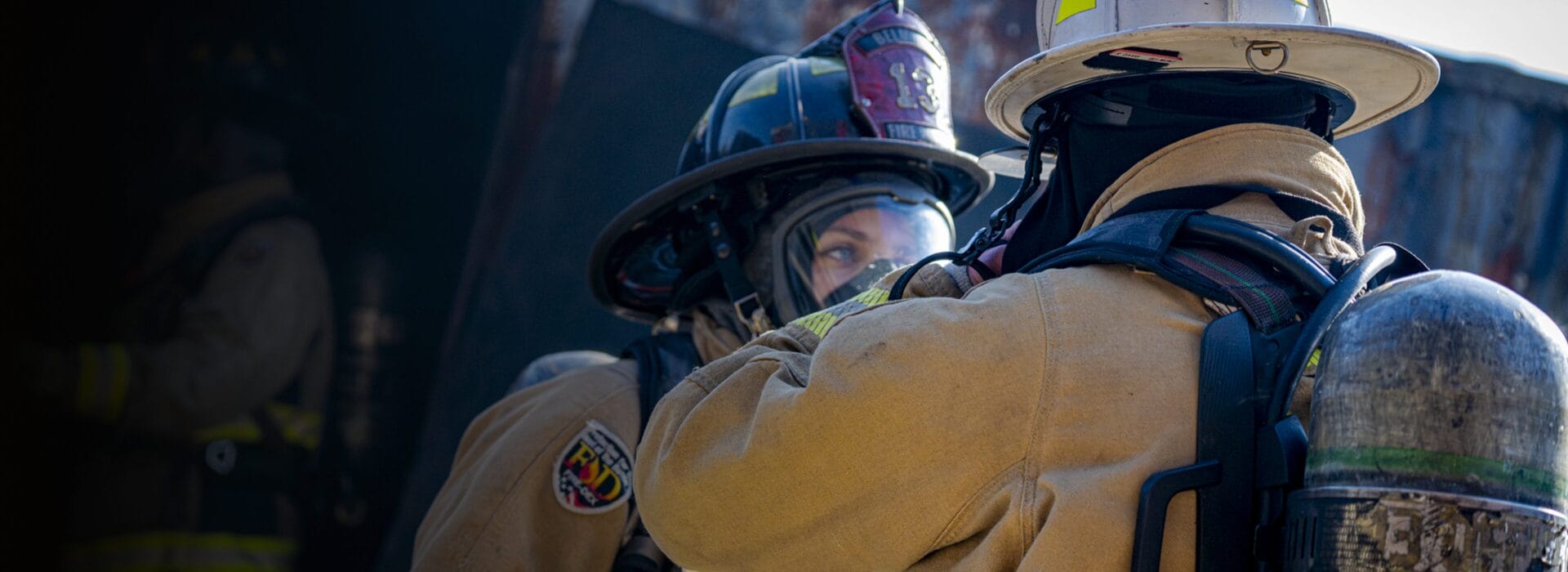 Two firefighters in full gear and helmets working together at an emergency scene