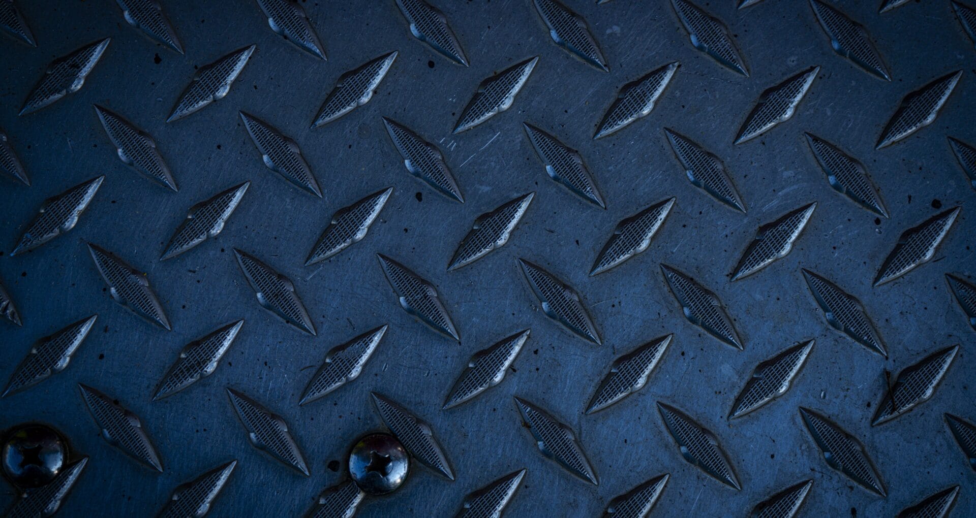 Close-up of a dark blue diamond-plate metal surface with bolt fasteners