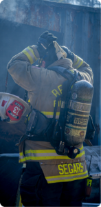 Firefighter in turnout gear adjusting gear amid smoke, with a Belmont Fire Rescue helmet clipped to their belt