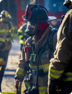 Firefighter in full protective gear with a face mask and helmet standing at an outdoor fire scene