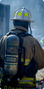 Rear view of a firefighter in turnout gear with an SCBA tank in a smoky outdoor setting