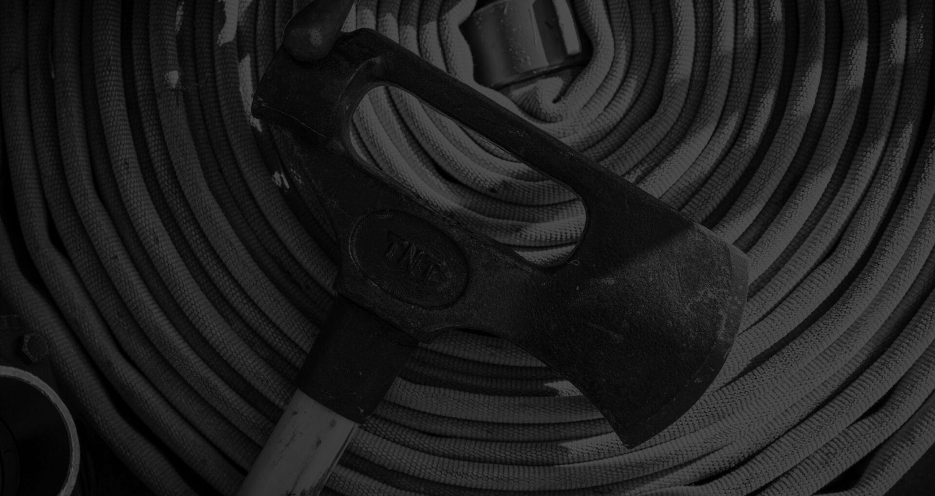 Black and white overhead view of a firefighter's axe resting on a coiled fire hose