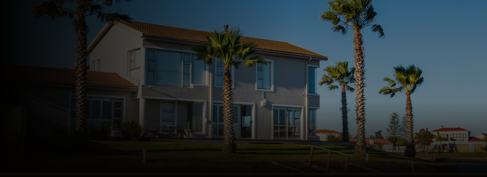 Two-story tan home with palm trees nearby.
