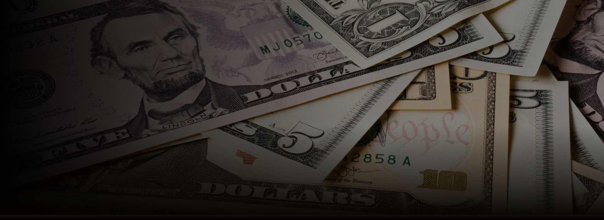 Dollar bills, including five-dollar bills, stacked and overlapping each other.
