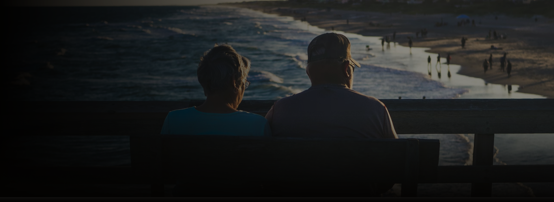 Older couple sitting together on a bench looking out at the beach.