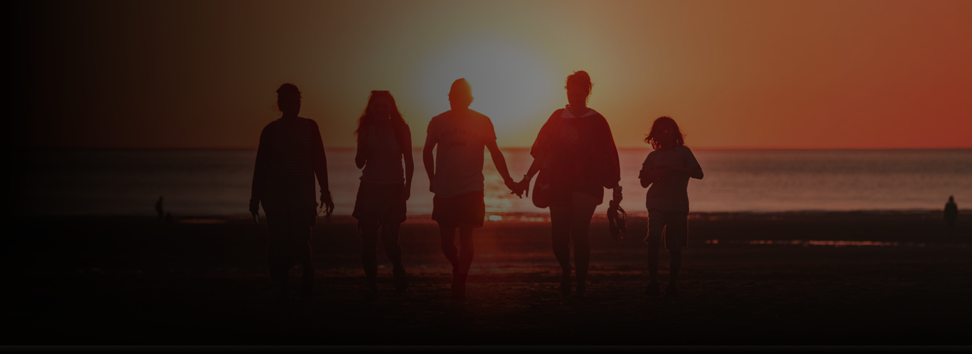 Family walking on the beach holding hands and looking out at the ocean.
