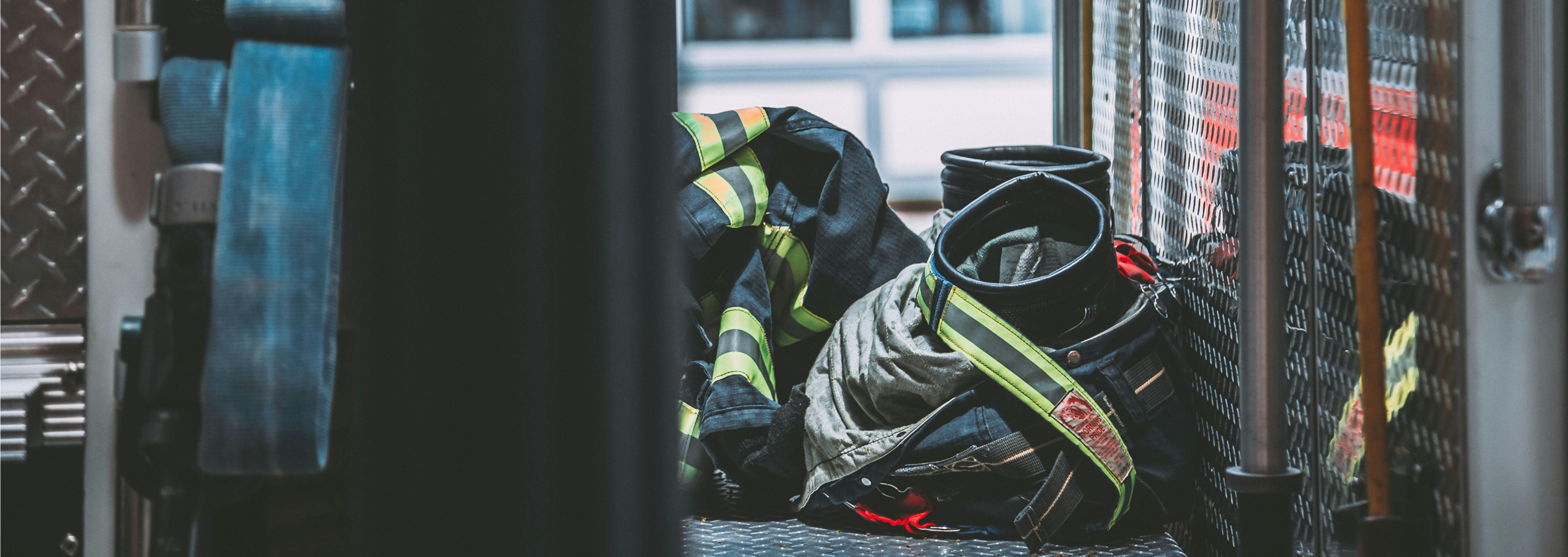 Firefighter turnout jacket and pants with yellow reflective strips resting on a firehouse floor next to a helmet