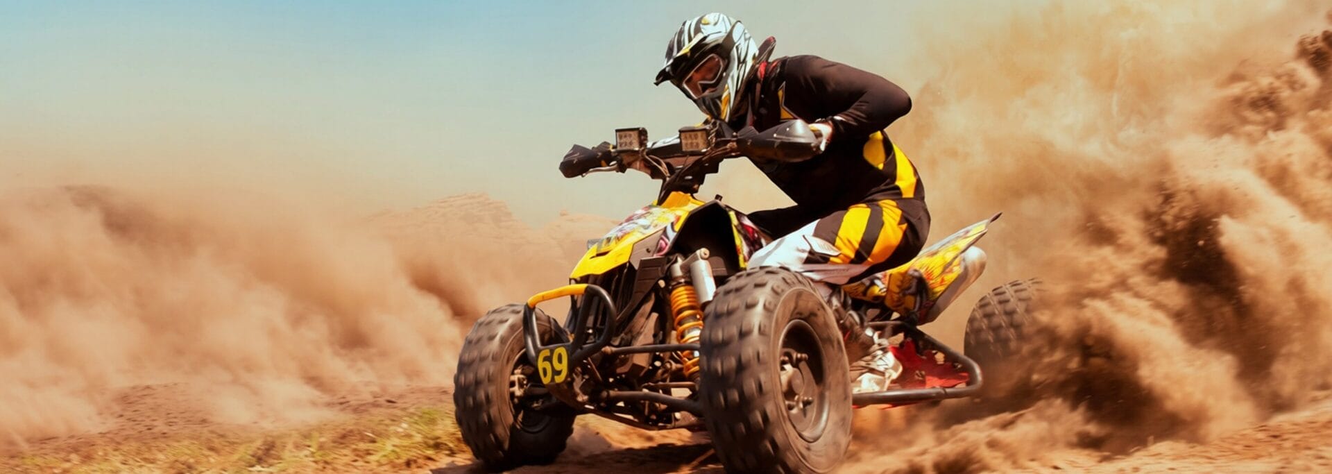 Rider in full gear racing a yellow ATV across a dusty off-road terrain