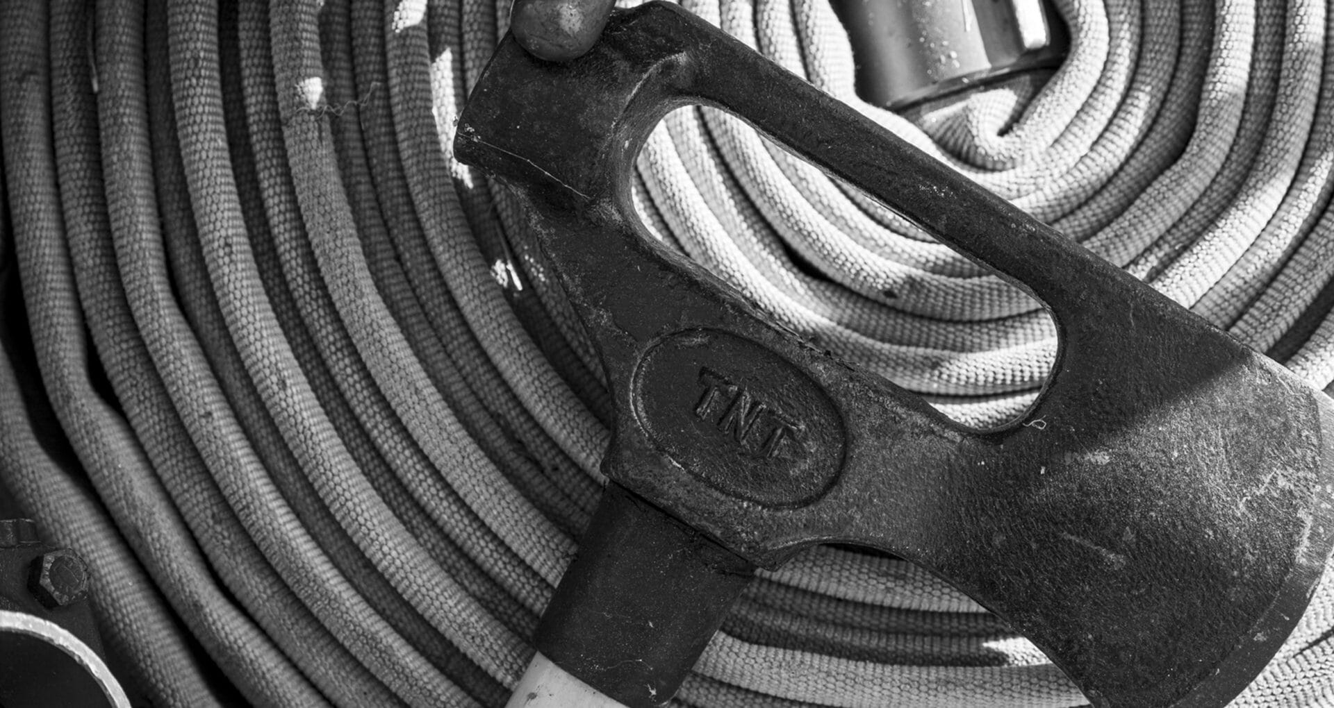 Black and white overhead view of a firefighter's axe resting on a coiled fire hose
