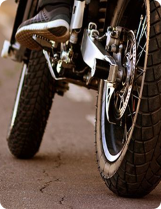 Low-angle close-up of a motorcycle rear wheel and foot peg on a road