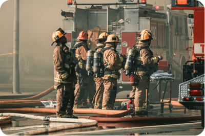 Group of five firefighters in full gear gathered around hose lines near a fire engine in smoky conditions