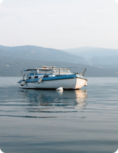White and blue motorboat anchored on a calm lake with forested mountains in the background