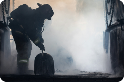 Firefighter in full protective gear working through heavy smoke at an active fire scene
