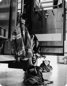 Turnout gear and a backpack staged beside a fire engine in a firehouse bay
