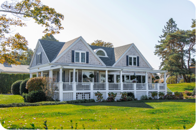 Large white Cape Cod style home with wraparound porch and well-maintained lawn