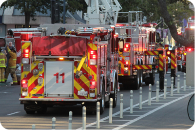 Column of fire engines with lights activated staged along an urban street