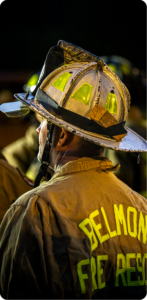 Belmont Fire Rescue firefighter viewed from behind wearing a worn helmet at a nighttime incident scene