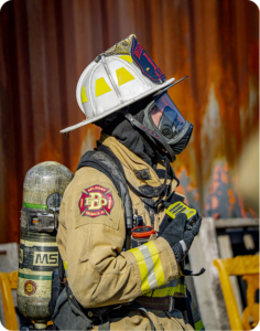 Belmont FPD firefighter in full protective gear and SCBA at a fire scene with flames visible in the background